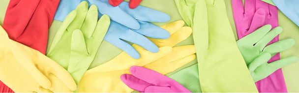 panoramic shot of scattered bright multicolored rubber gloves on green background - 写真・画像