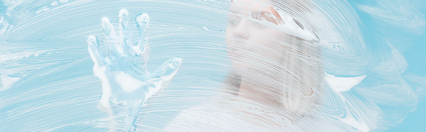 tiro panorâmico de jovem mulher em luva de borracha tocando vidro coberto com espuma no fundo azul
 - Foto, Imagem