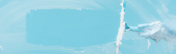 plano panorámico de mujer en guante de goma vidrio de limpieza con escobilla sobre fondo azul
 - Foto, Imagen