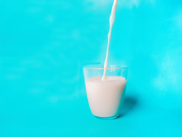 Close-up shot van melk gieten in glas op blauw oppervlak - Foto, afbeelding