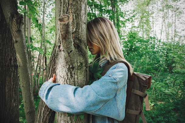 жінка з рюкзаком обіймає дерево в лісі
  - Фото, зображення