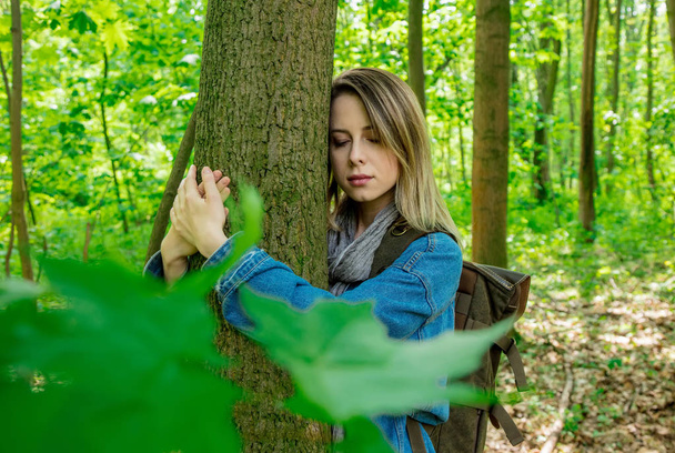 Frau mit Rucksack umarmt Baum im Wald  - Foto, Bild