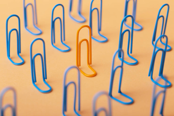 orange clip among the blues, unlikeness to others, the concept of individuality, optimism, creative idea with office paper clips, concept of psychology - Foto, immagini