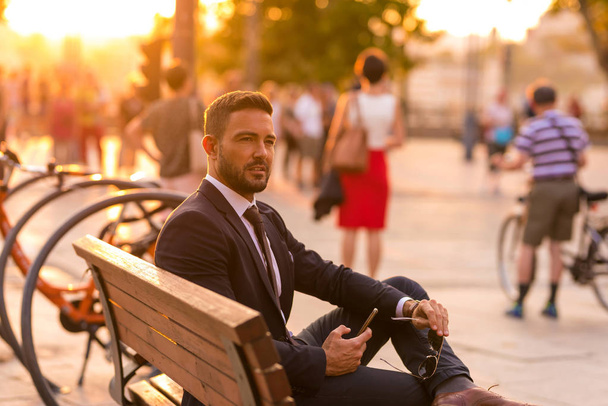 A businessmen sitting on a bench and using his smartphone - Фото, изображение