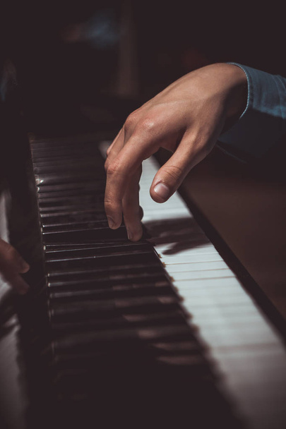 one male hand on the piano. The palm lies on the keys and plays the keyboard instrument in the music school. student learns to play. hands pianist. black dark background. vertical - Foto, afbeelding