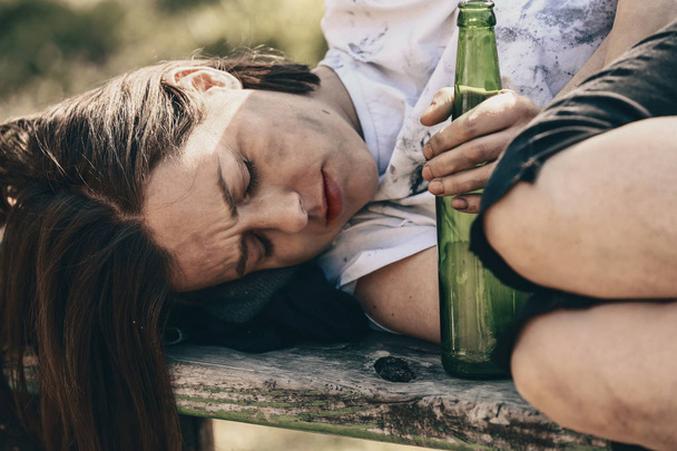 屋外のベンチに横たわっているボトルを持つ貧しいホームレスの女性 - 写真・画像
