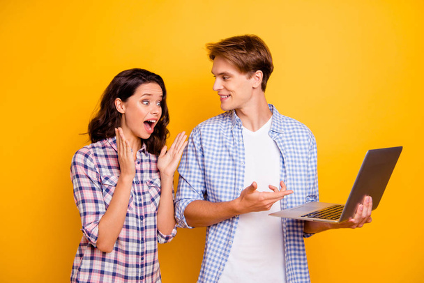 Close up photo of pair teens he him his she her lady boy with computer in hands great news won play pen-friend comes to visit them wearing casual plaid shirts outfit isolated on yellow background - 写真・画像