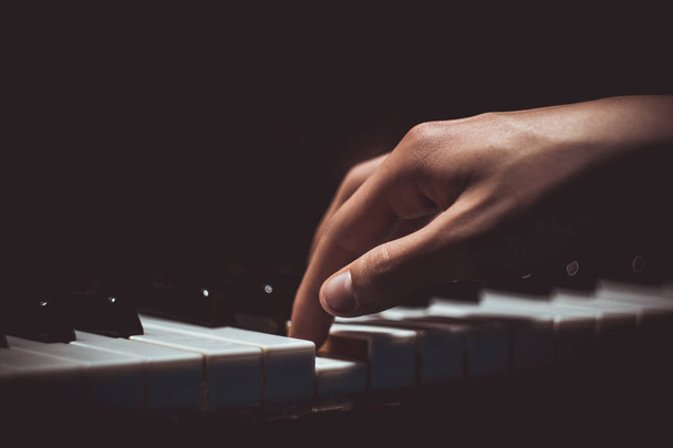 one male hand on the piano. The palm lies on the keys and plays the keyboard instrument in the music school. student learns to play. hands pianist. black dark background - Foto, afbeelding