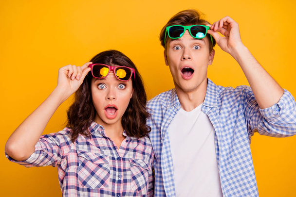 Close up photo of pair in raised up summer glasses specs he him his she her lady boy showing shock staring  with open eyes and mouth wearing casual plaid shirts outfit isolated on yellow background - Zdjęcie, obraz