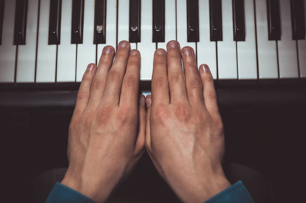 two male hands on the piano. palms lie on the keys and play the keyboard instrument in the music school. student learns to play. hands pianist. black dark background. top view - 写真・画像