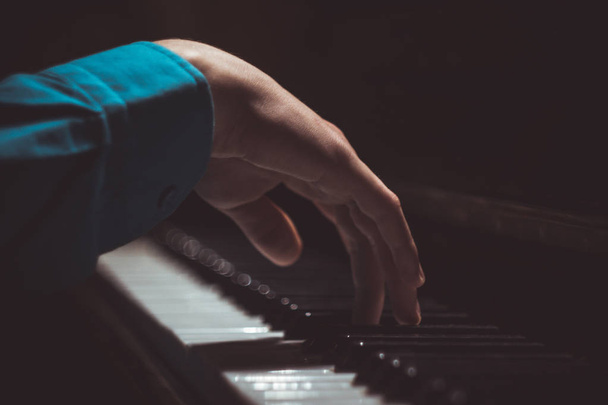 one male hand on the piano. The palm lies on the keys and plays the keyboard instrument in the music school. student learns to play. hands pianist. black dark background - Photo, image