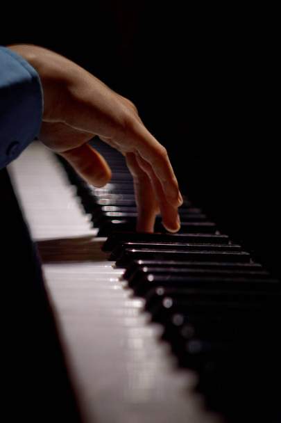 one male hand on the piano. The palm lies on the keys and plays the keyboard instrument in the music school. student learns to play. hands pianist. black dark background. vertical - Photo, image