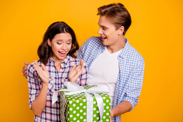 Close up photo of pair in love he him his she her lady boy husband making surprise for wife large giftbox wearing casual plaid shirts outfit isolated on yellow background - Photo, Image