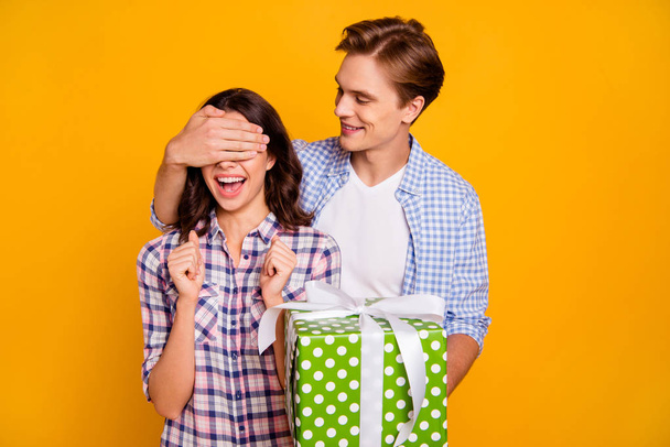 Close up photo of pair in love he him his she her lady boy hiding eyes before giving big bow with sweets wearing casual plaid shirts outfit isolated on yellow background - Fotoğraf, Görsel