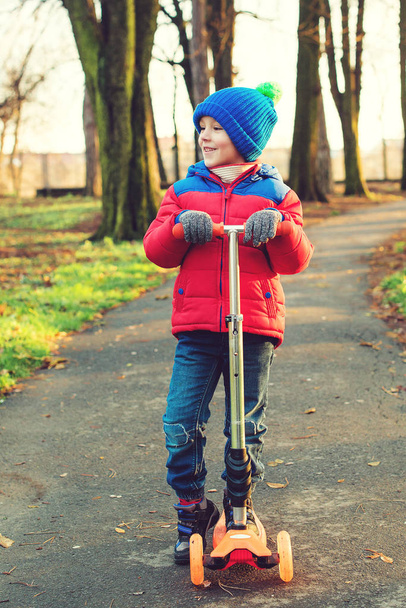 Srandovní chlapeček jezdíš na skútru na chladném podzim. Dětský sport venku. - Fotografie, Obrázek