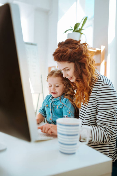 Woman working remotely spending time with her lovely daughter - Foto, afbeelding