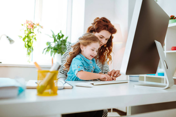 Girl sitting near computer with her mother working at home - Foto, Bild