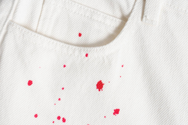 White jeans in red paint splatter. Closeup denim texture. Dry cleaning required. - Photo, Image