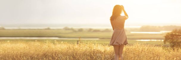 dreamy girl in a field at sunset, a young woman in a haze from the sun enjoying nature, romantic style - Foto, imagen