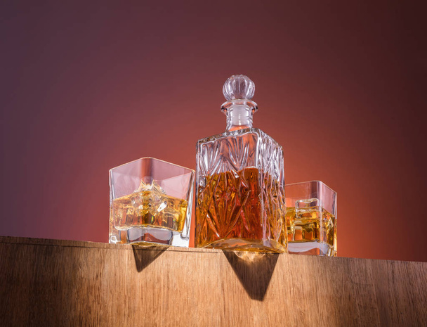 Old fashion glass and carafe with the alcohol, whisky drink on warm, dark orange background and wood - Foto, Imagem