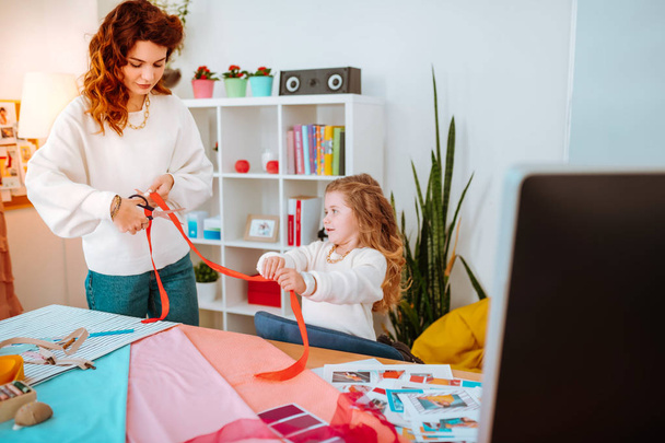 Fashion designer cutting red ribbon with her little girl helping her - Photo, Image