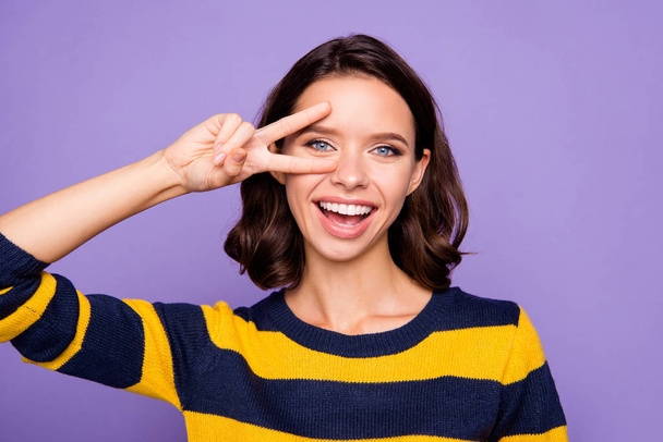 Close up photo beautiful she her lady arm hand fingers raised near eye v-sign symbol say hi relatives friends peaceful nice person wear blue yellow striped pullover isolated violet purple background - Foto, imagen