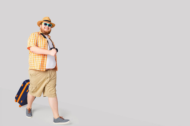 Fat funny man with a suitcase smiling on a gray background. - Photo, Image