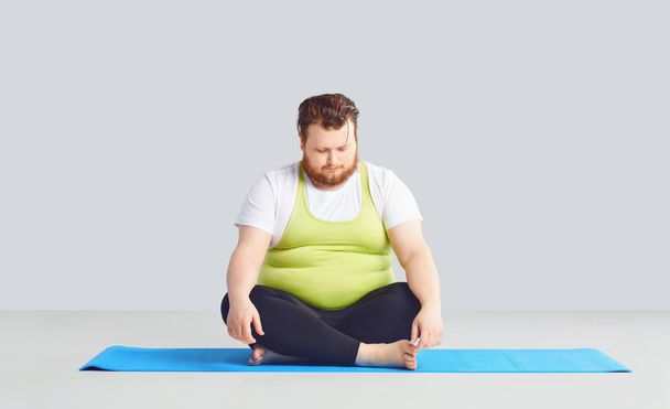 A fat unhappy man in yoga clothes on a gray background. - Foto, Imagem