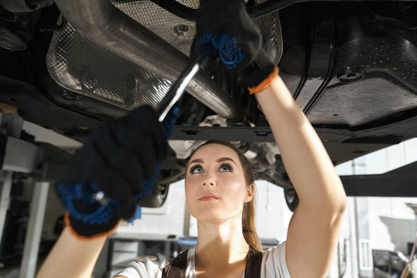 Young woman fixing undercarriage with wrench. - Fotoğraf, Görsel
