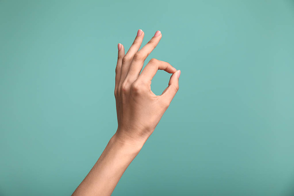 Vrouwelijke hand tonen OK gebaar op kleur achtergrond - Foto, afbeelding