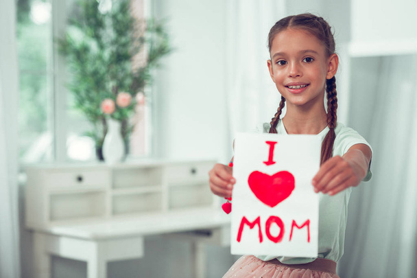 Nice-looking Afro-American girl showing picture with I love mom sign. - Foto, Imagem