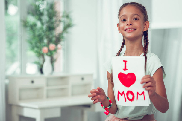 Beaming child showing a painting with I love mom sign. - Foto, immagini