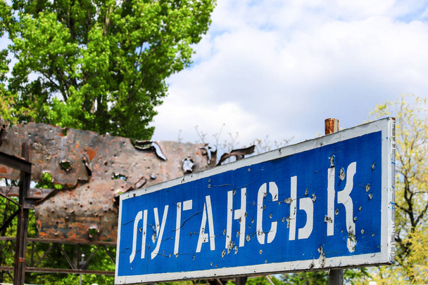 ウクライナのルガンスクの碑文と青い道路標識は、ドンバス、紛争東ウクライナ、ウクライナ戦争の戦争中に弾丸でパンチ - 写真・画像