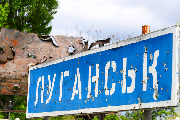 Sinal de estrada azul com a inscrição em ucraniano Lugansk, perfurado por balas durante a guerra no Donbass, conflito Leste da Ucrânia, guerra ucraniana
 - Foto, Imagem