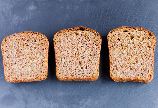 drie stukjes rogge Borodino brood op een zwarte stenen achtergrond - Foto, afbeelding