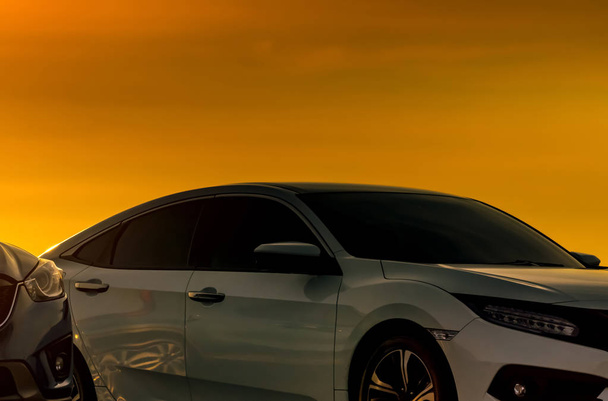 美しいオレンジ色の夕日の空と駐車場に駐車豪華でモダンなデザインの白い車の正面図。自動車産業。ロードトリップ旅行。仕事の後に夕日の空を見るための駐車車.  - 写真・画像
