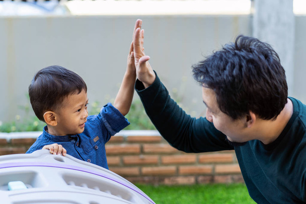 Asian single dad with son are playing and give me five together when living in front lawn for Self learning or home school, Family and single father concept, selective focus - Photo, Image