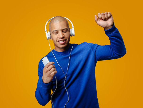 Knappe Afro-Amerikaanse man luisteren naar muziek op kleur achtergrond - Foto, afbeelding