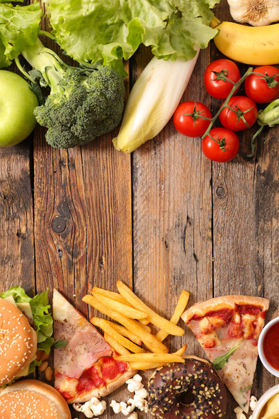 Top view of healthy eating against fast food and pastry on wooden table  - Photo, Image