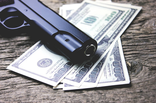 a gun with money on a wooden table - Фото, зображення