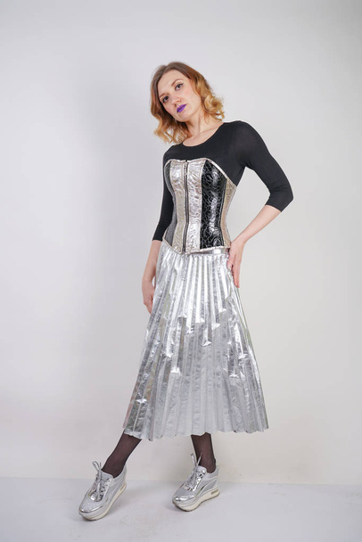 beautiful caucasian girl wearing futuristic pvc corset and plaid metallic skirt with mirrored running shoes on white background in the studio - Foto, afbeelding