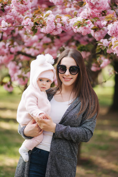 Mutter mit kleiner Tochter im Park in der Nähe des Sakura-Baumes - Foto, Bild