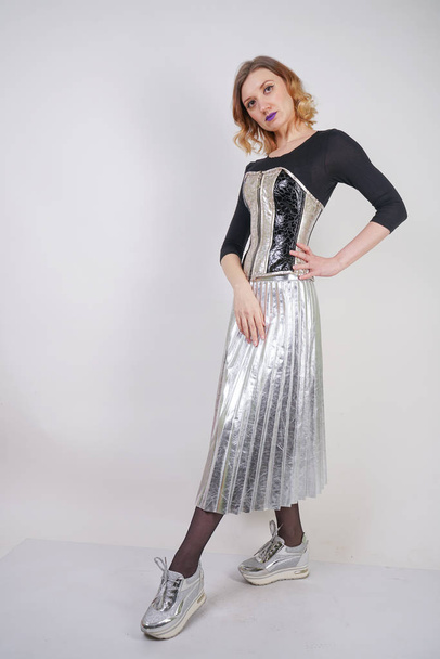 beautiful caucasian girl wearing futuristic pvc corset and plaid metallic skirt with mirrored running shoes on white background in the studio - Photo, image