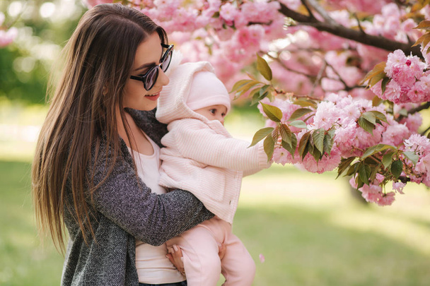 Äiti näyttää kuuset aikaa tyttärelleen vaaleanpunainen puu. Happy Baby Hold haara Sakura. Sivukuva
 - Valokuva, kuva