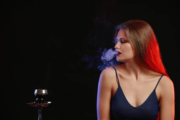 Νεαρή γυναίκα που καπνίζει ναργιλέ σε σκούρο φόντο - Φωτογραφία, εικόνα