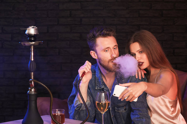 Young couple taking selfie while smoking hookah in cafe - Photo, Image