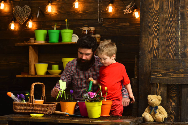 Father and son. Fathers day. happy gardeners with spring flowers. bearded man and little boy child love nature. Family day. Greenhouse. Flower care watering. Soil fertilizers. Positive florist - Foto, Imagen
