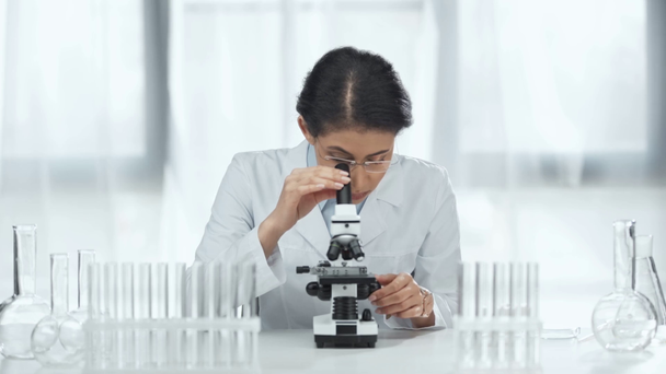 african american scientist in glasses looking at sample through microscope in lab  - Metraje, vídeo