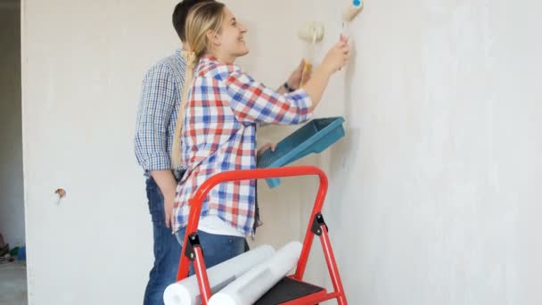 Video of young man with his wife painting walls with white paint in new house - Footage, Video