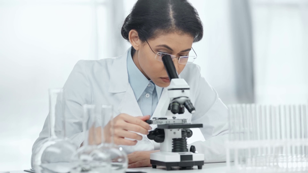 african american scientist in glasses writing on clipboard while looking at sample through microscope in lab  - Πλάνα, βίντεο